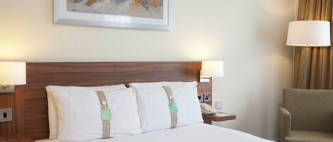 A hotel room with a large bed, two bedside lamps, a nightstand with a phone, a chair, and a painting on the wall.