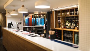 A bar area with a long counter, multiple hanging pendant lights, and shelves stocked with bottles and glasses. - Holiday Inn Stoke on Trent M6, Jct 15 by IHG (Newcastle-Under-Lyme)