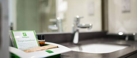 Ein Badezimmer-Waschtisch mit Waschbecken, Spiegel und einer Aufstellung von Toilettenartikeln.