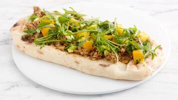 Een platbrood met toppings op een wit bord.