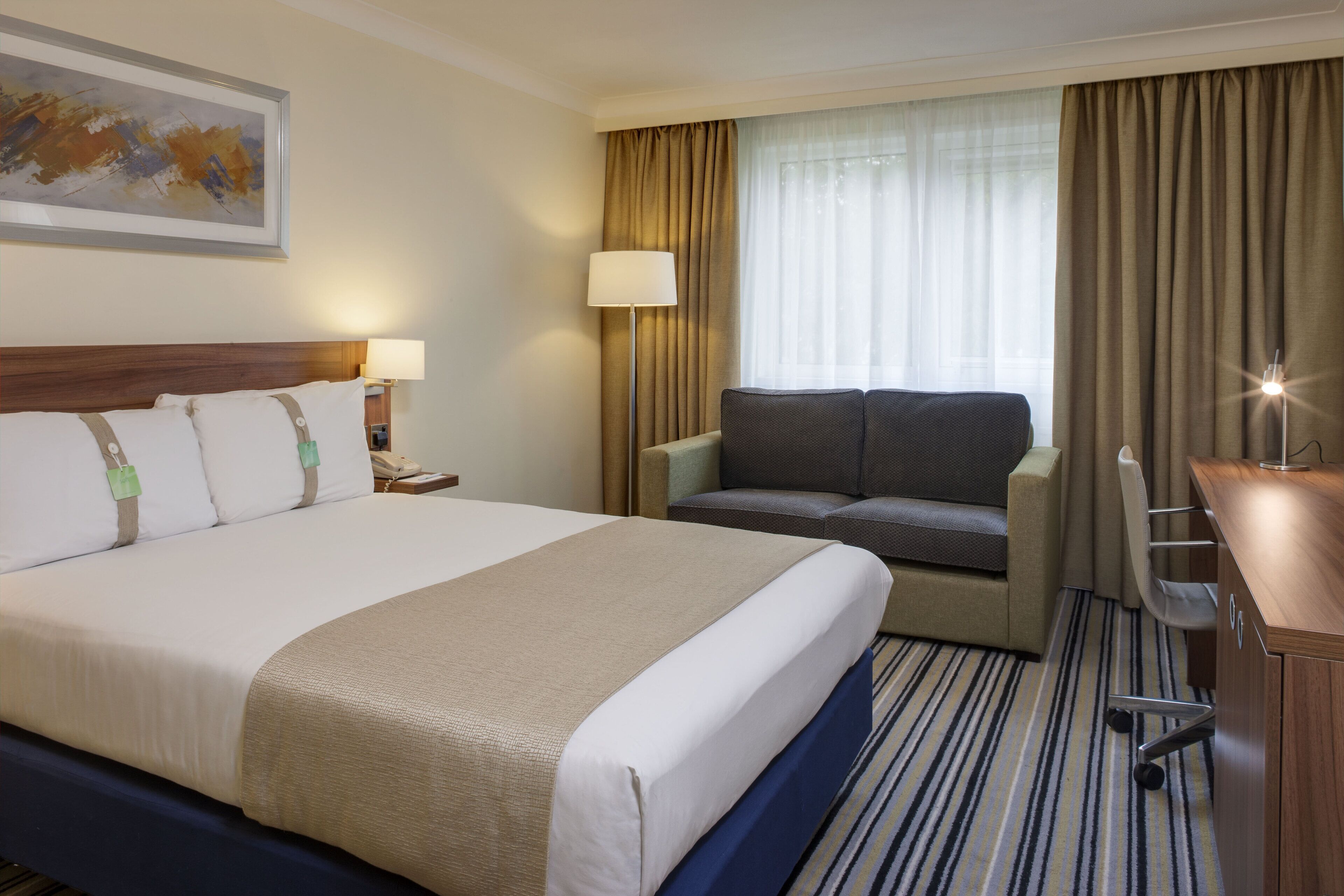A hotel room with a large bed, a sofa, a desk, and a chair.