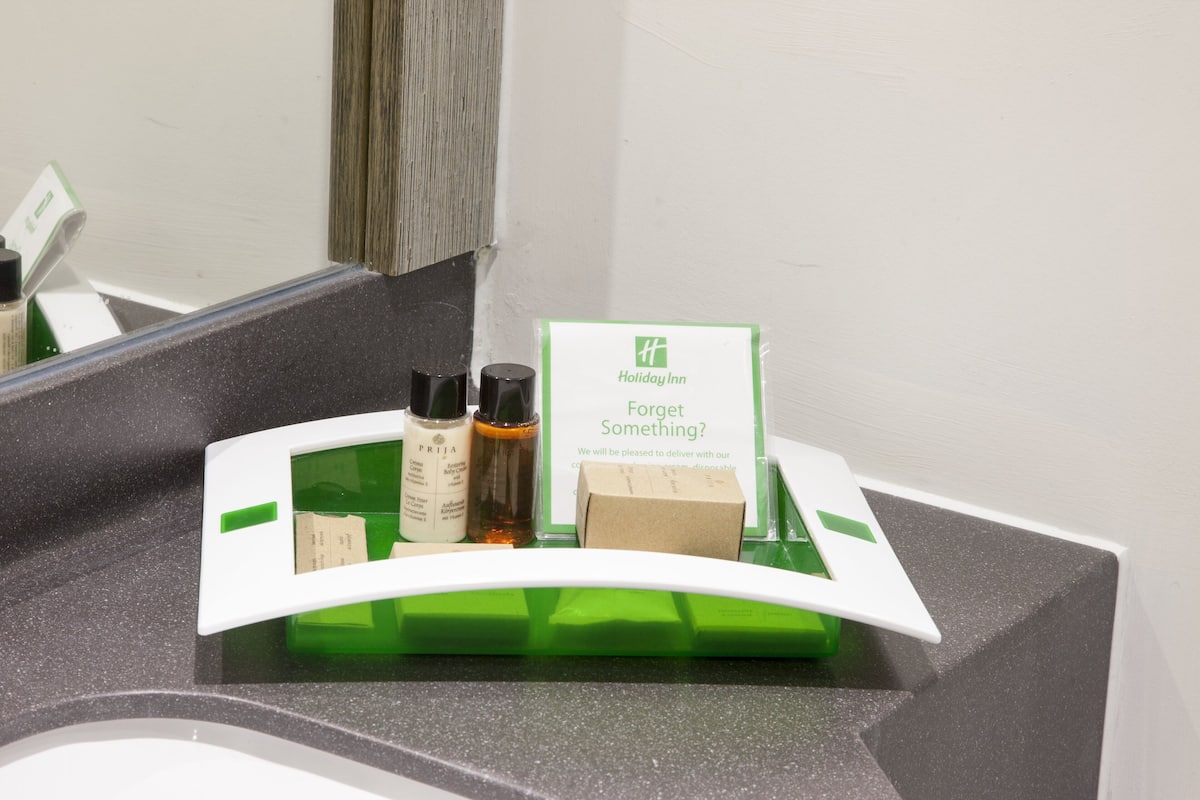 A bathroom counter with a green and white tray holding toiletries, a sign for Holiday Inn, and a mirror.