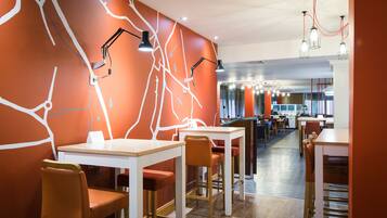 Un restaurante moderno con mesas blancas y sillas anaranjadas, que presenta un diseño de pared único con líneas blancas y un techo rojo.