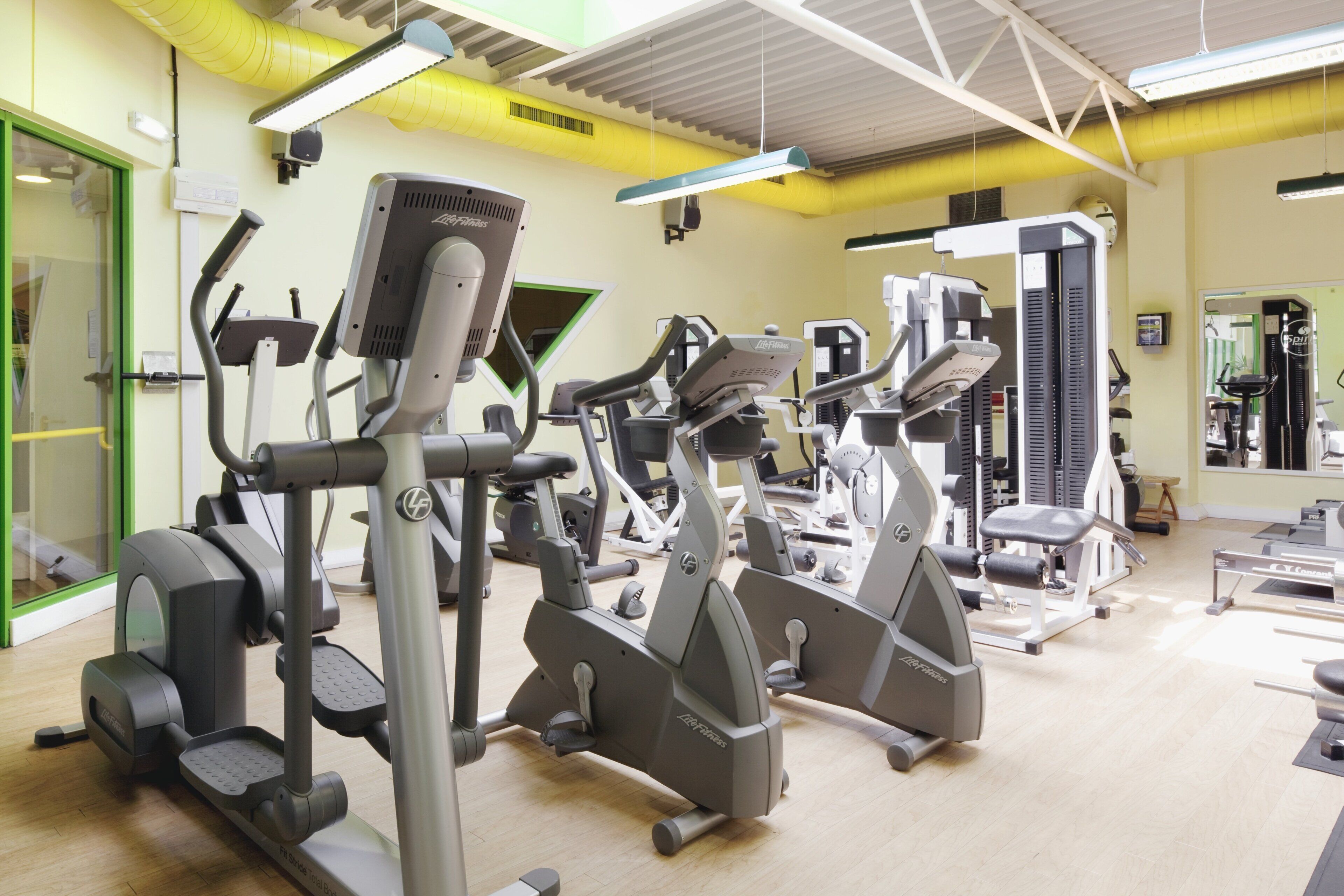 A gym with various exercise machines, a mirrored wall, and a green door.