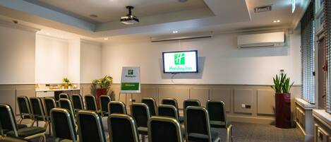 A conference room with rows of chairs, a projector screen, and a Holiday Inn sign.