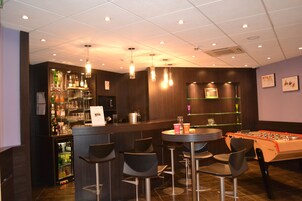 Un espace bar avec des tabourets, une table de baby-foot et un comptoir bien garni de bouteilles.