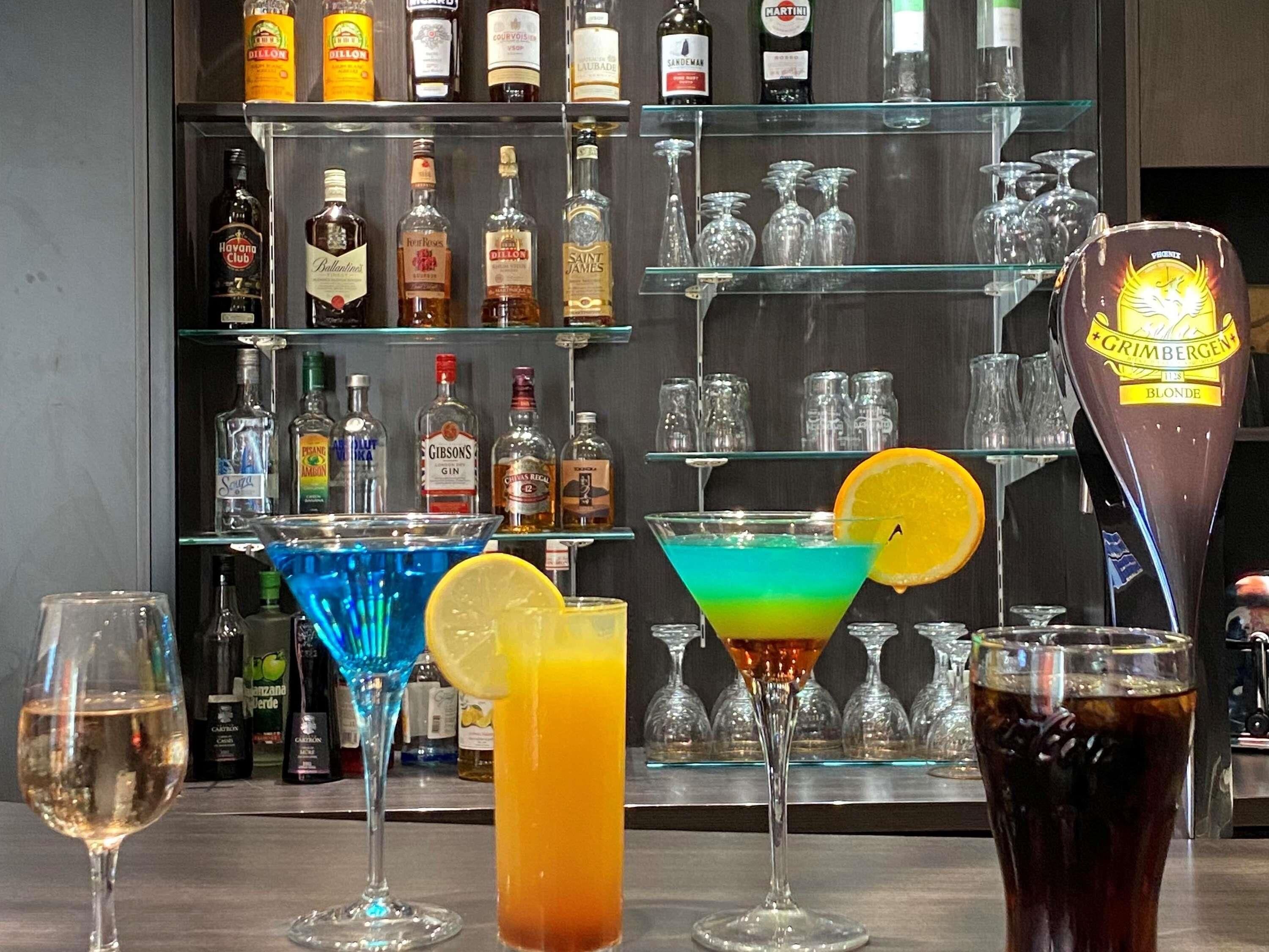 A bar area with various bottles and glasses, including a blue cocktail and a martini glass with an orange slice.