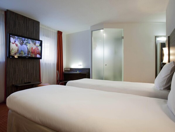 A hotel room with two beds, a television, a desk, and a glass-enclosed closet.