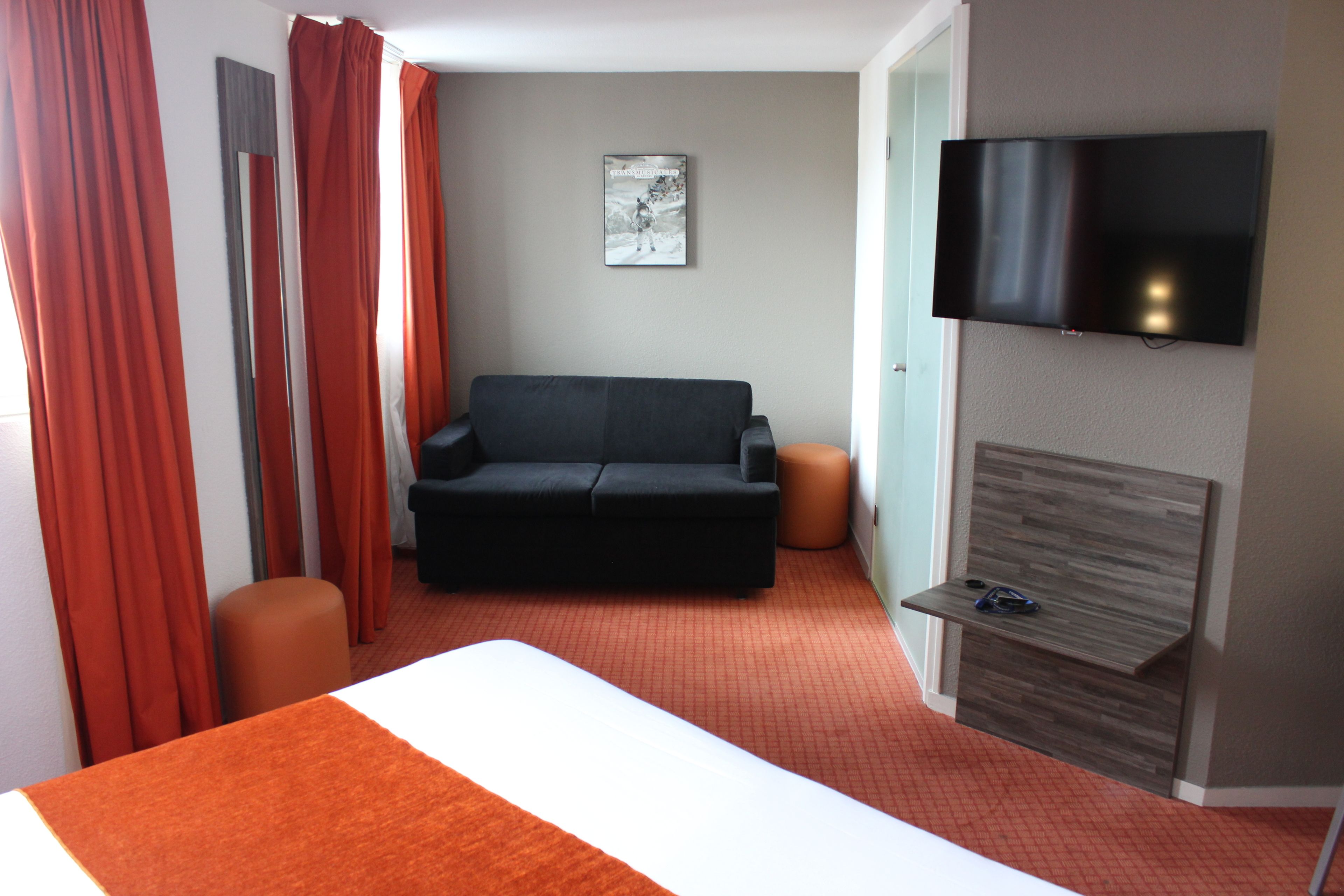 A hotel room with a bed, a sofa, a TV, and a small table.