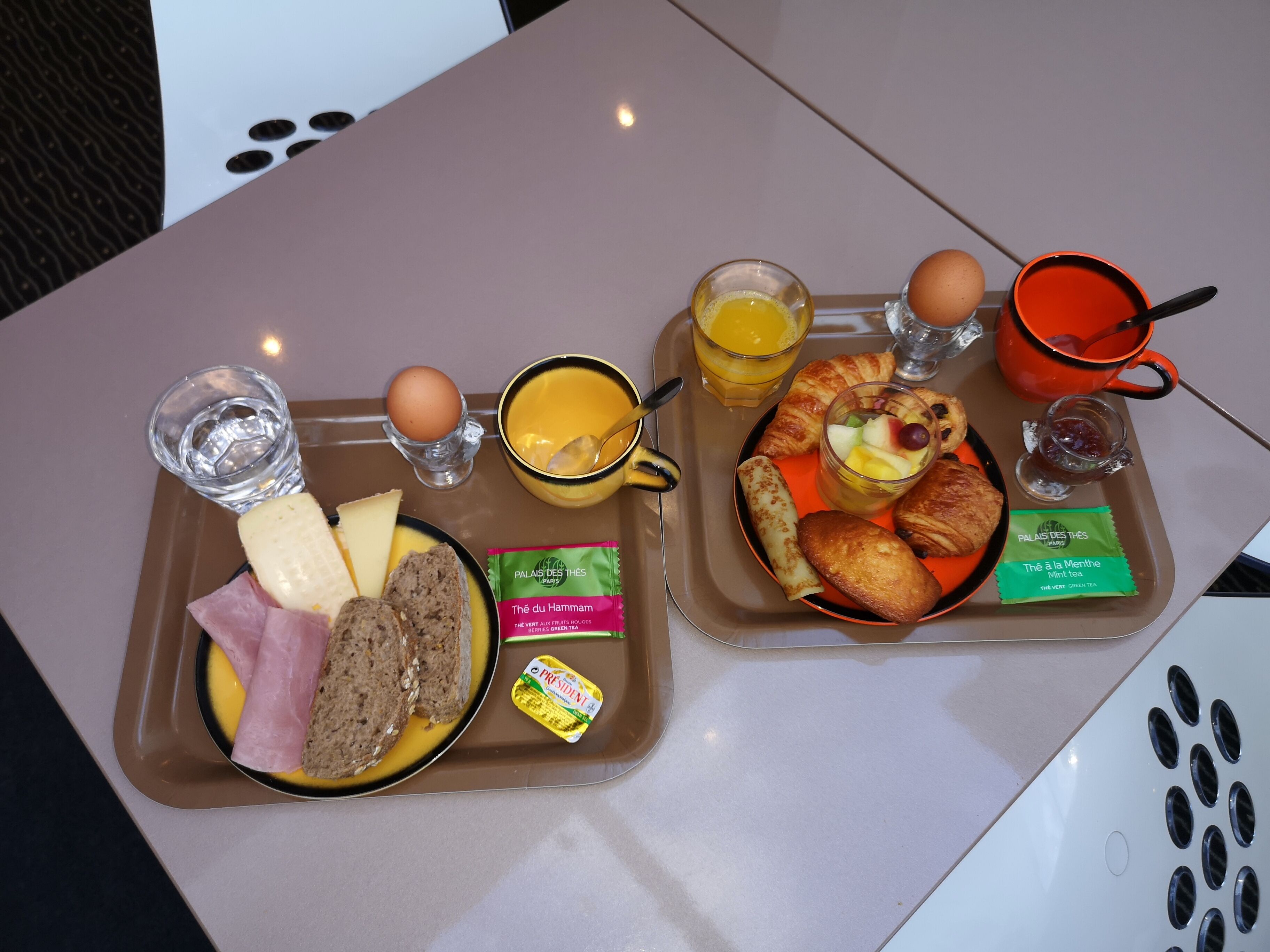 A breakfast tray with croissants, eggs, cheese, ham, and juice.