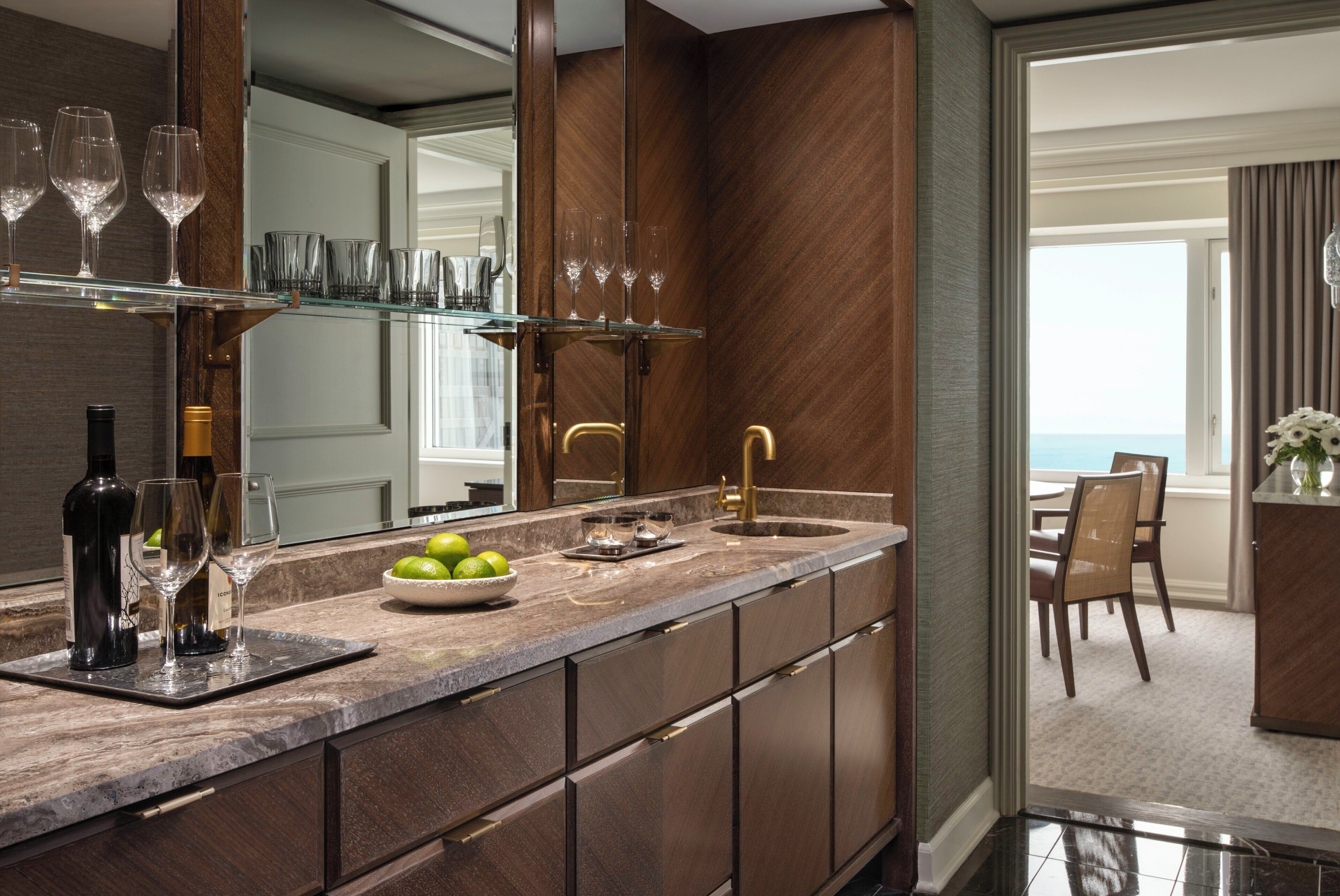 A modern kitchen with a marble countertop, wine glasses, and a bowl of limes.