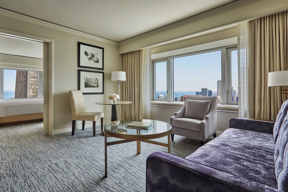 A hotel room with a bed, two armchairs, a coffee table, and a view of the city.