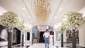 A couple walking through a spacious lobby with marble flooring, large white floral arrangements, and a modern staircase in the background. - Four Seasons Hotel Chicago (Chicago)