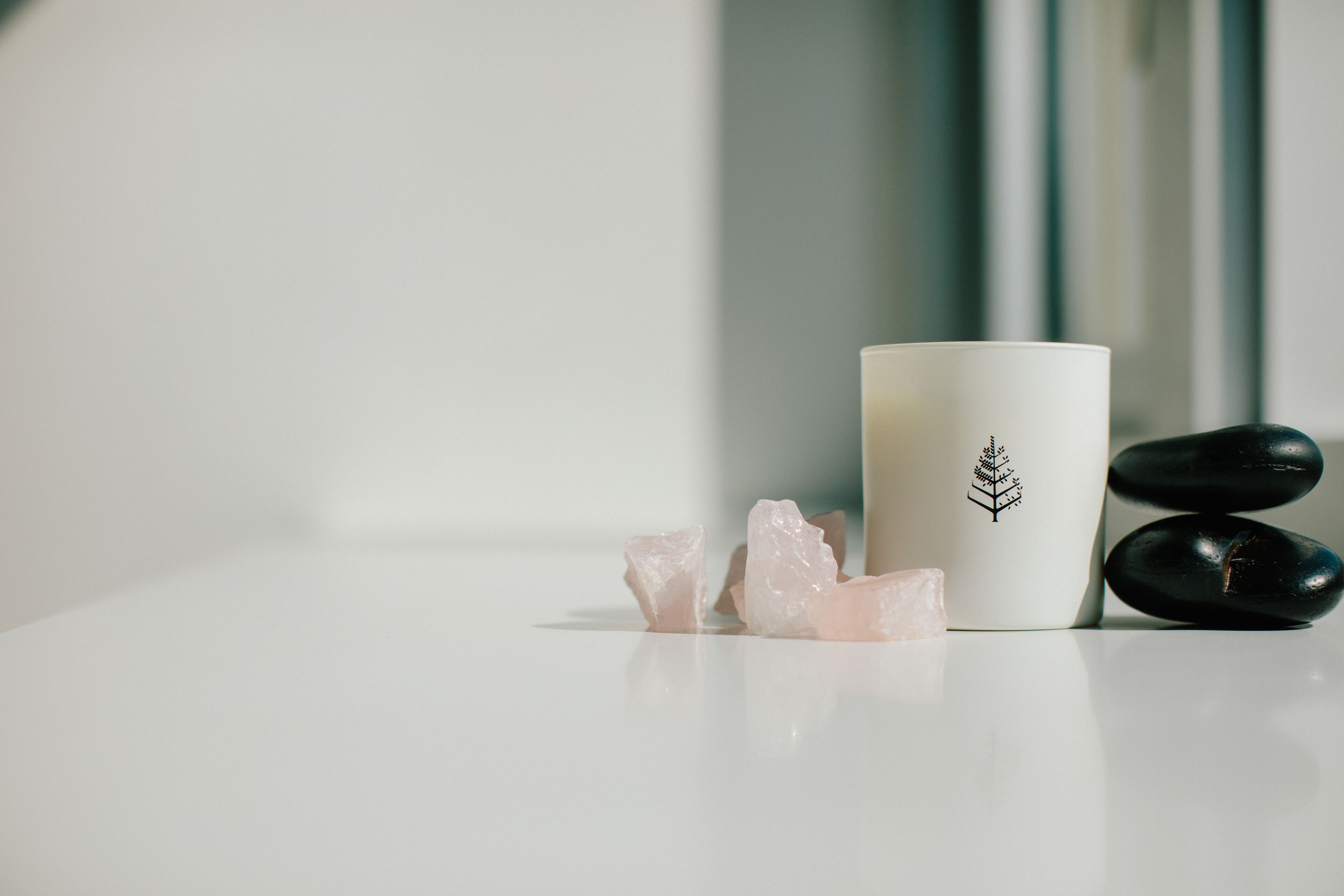 Una superficie bianca con una candela bianca, due pietre nere e alcuni cristalli rosa.