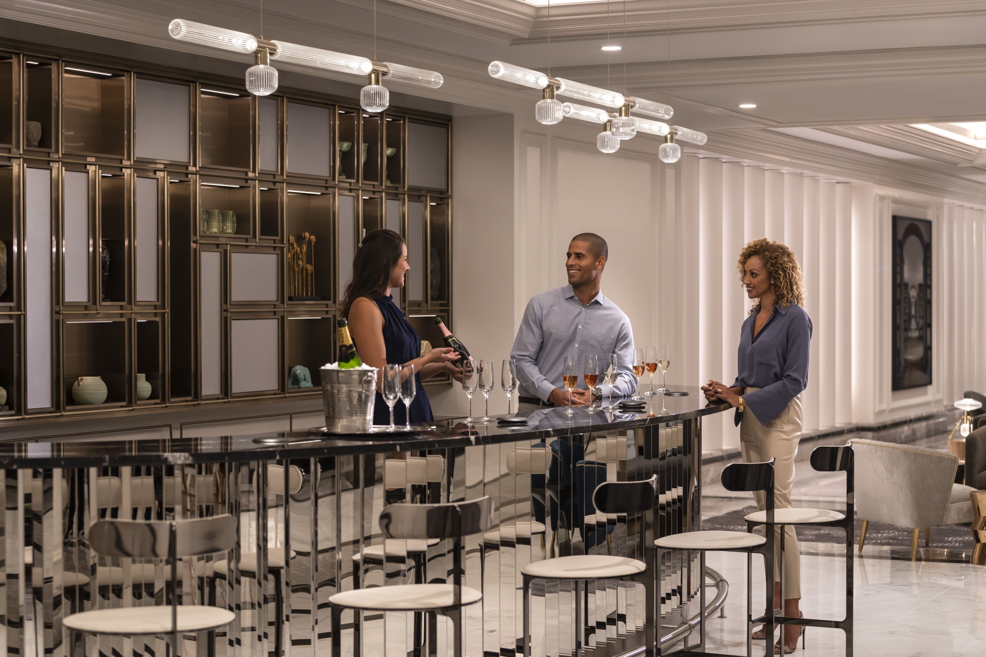 Uma área de bar moderna com divisória de vidro, banquetas e um candelabro.