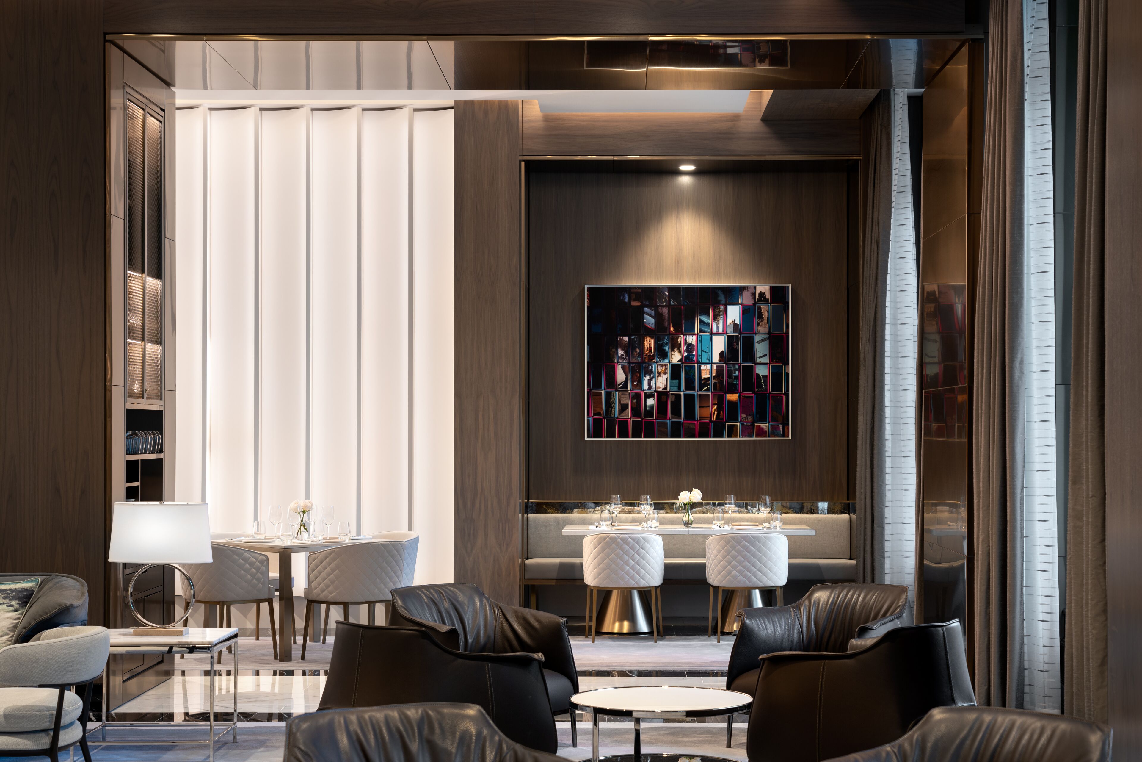 Un intérieur moderne comprenant un coin repas, des sièges en cuir et une grande œuvre d’art abstraite accrochée au mur.