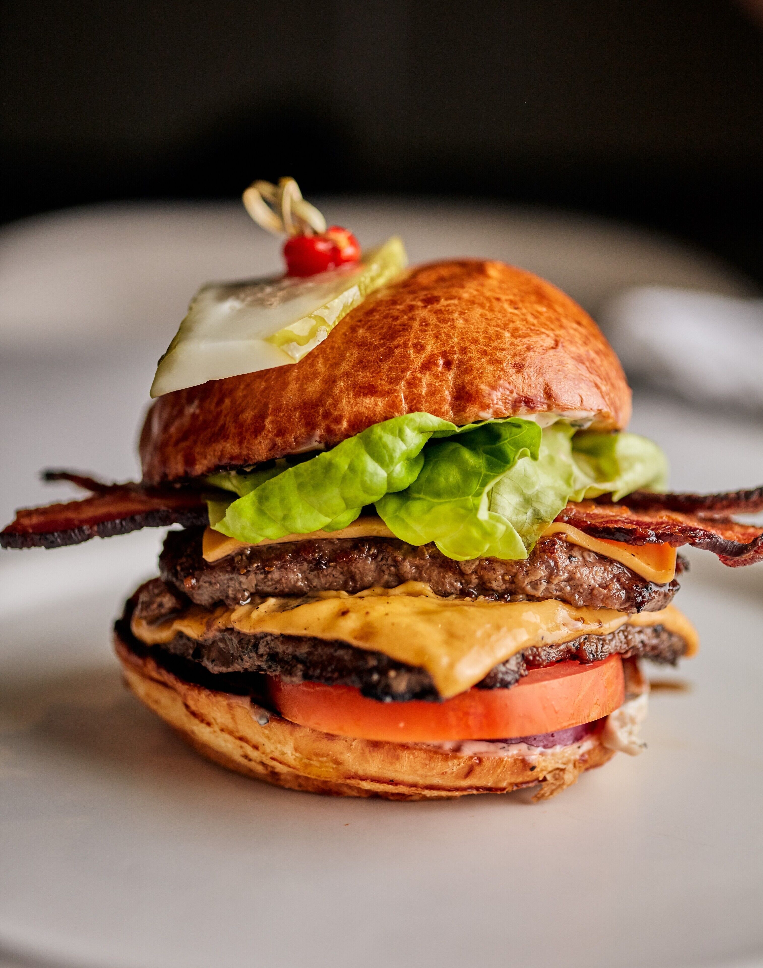 A close-up of a burger with lettuce, tomato, cheese, and bacon.