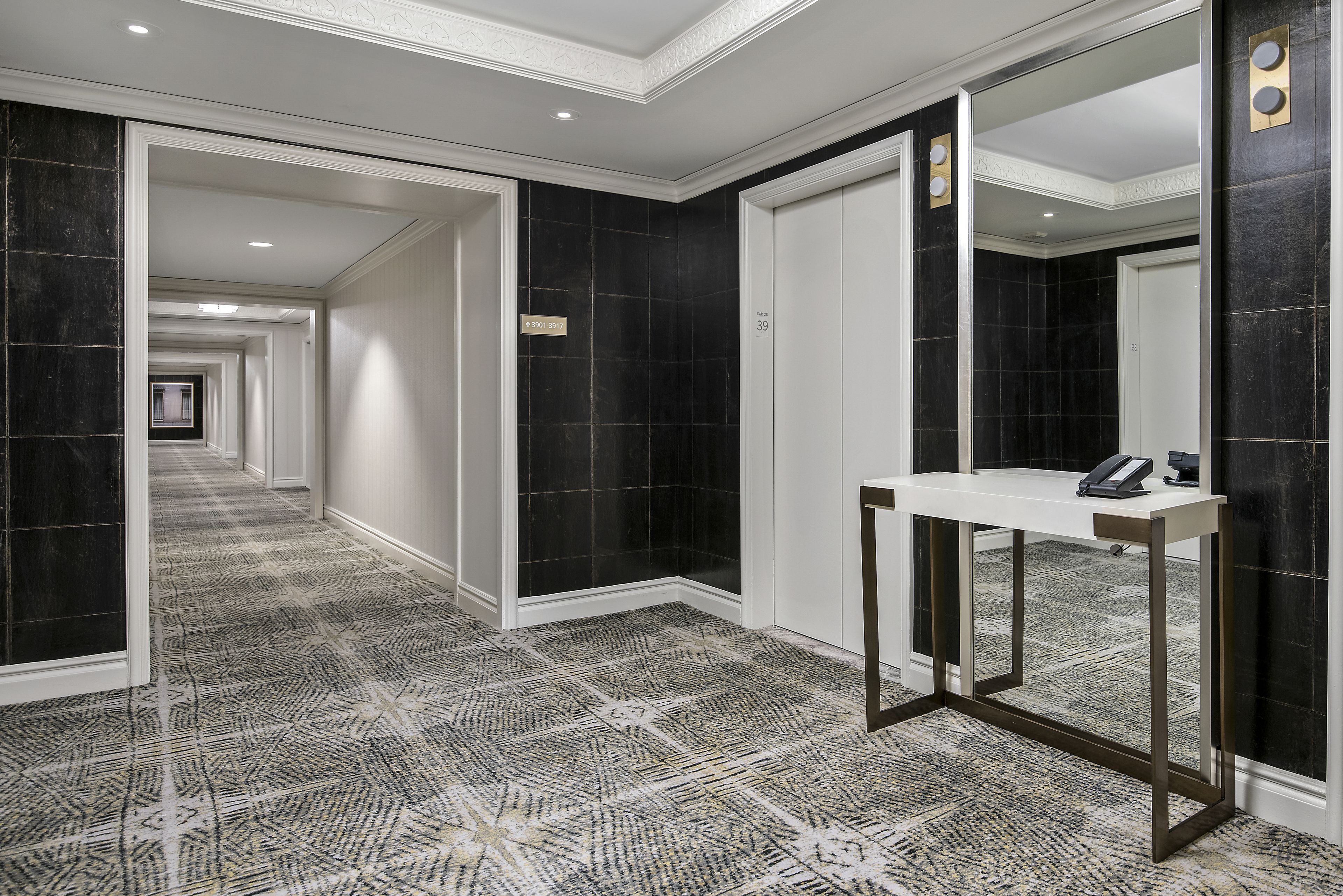 A hallway with black and white patterned carpet, a white reception desk, and a mirror.