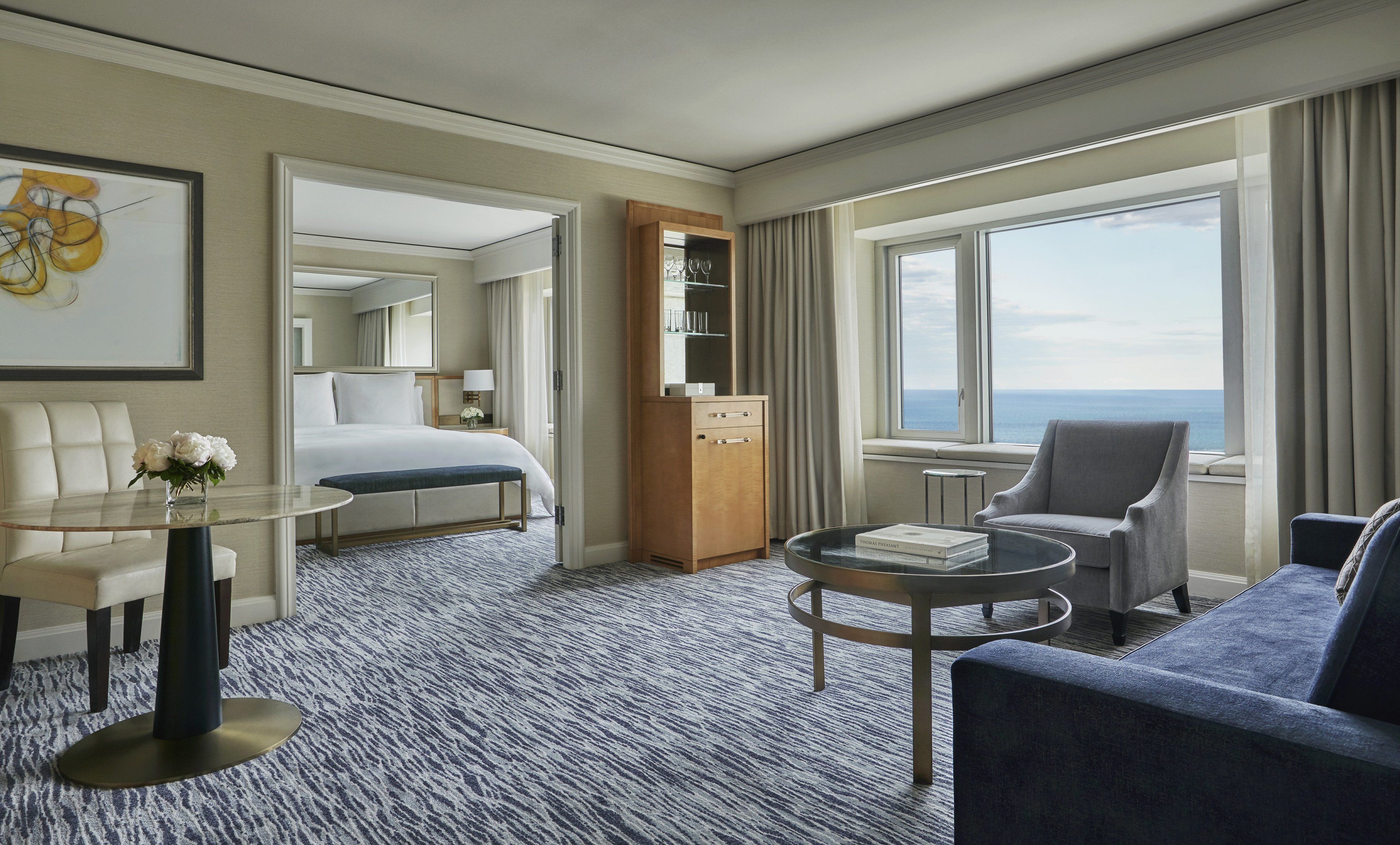 A hotel room with a bed, a seating area with a coffee table, a desk, and a view of the ocean.