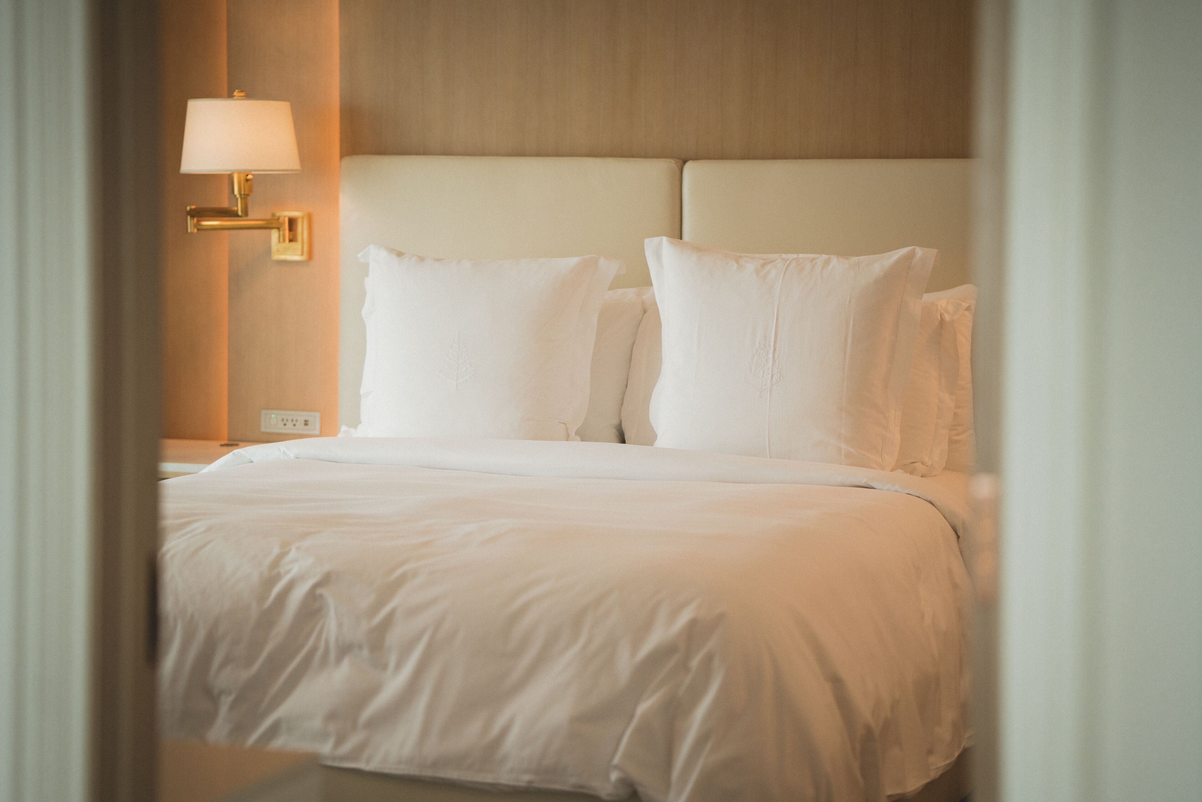 Una cama bien hecha con sábanas blancas y una lámpara de pared.