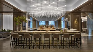 A modern bar area with a central bar and multiple stools, surrounded by a high ceiling with a decorative light fixture. - Four Seasons Hotel Chicago (Chicago)