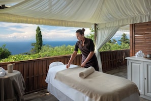 A massage room with a wooden deck, a massage table, and a view of the sea.