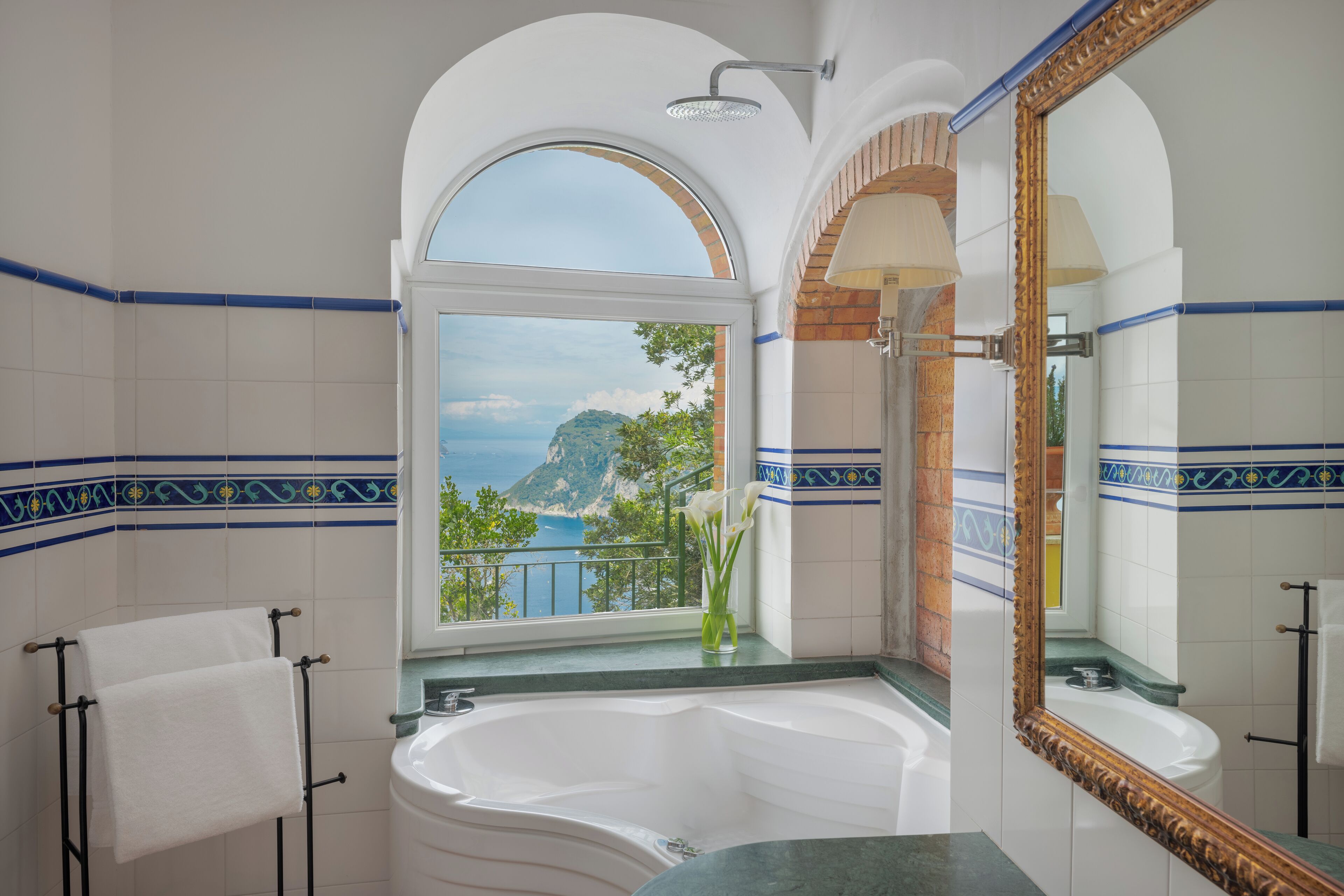 Un baño con una bañera grande, una ventana con vista al mar y un espejo con marco decorativo.