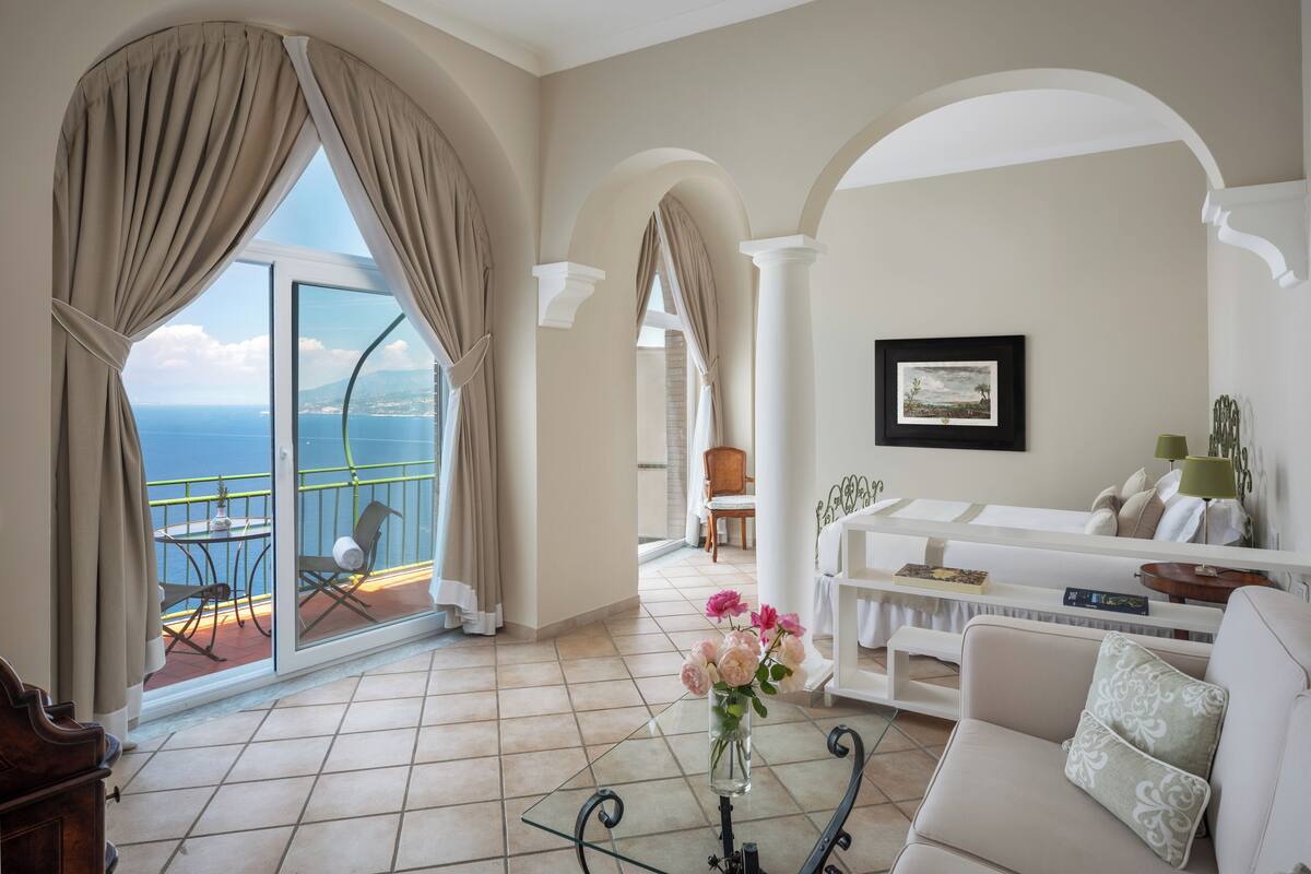 A spacious living area with a balcony, a white sofa, a coffee table, and a vase of flowers.