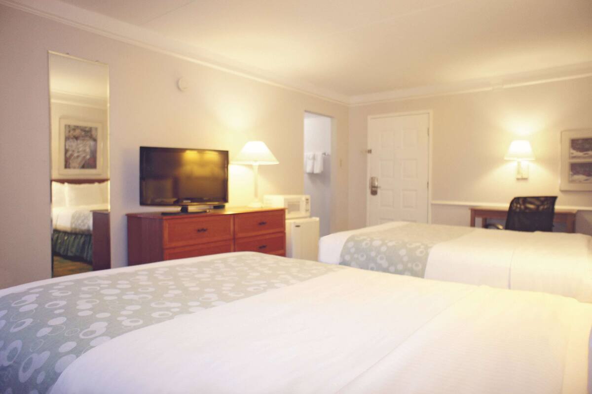 A hotel room with two beds, a television, a desk with a chair, and two wall-mounted lamps.