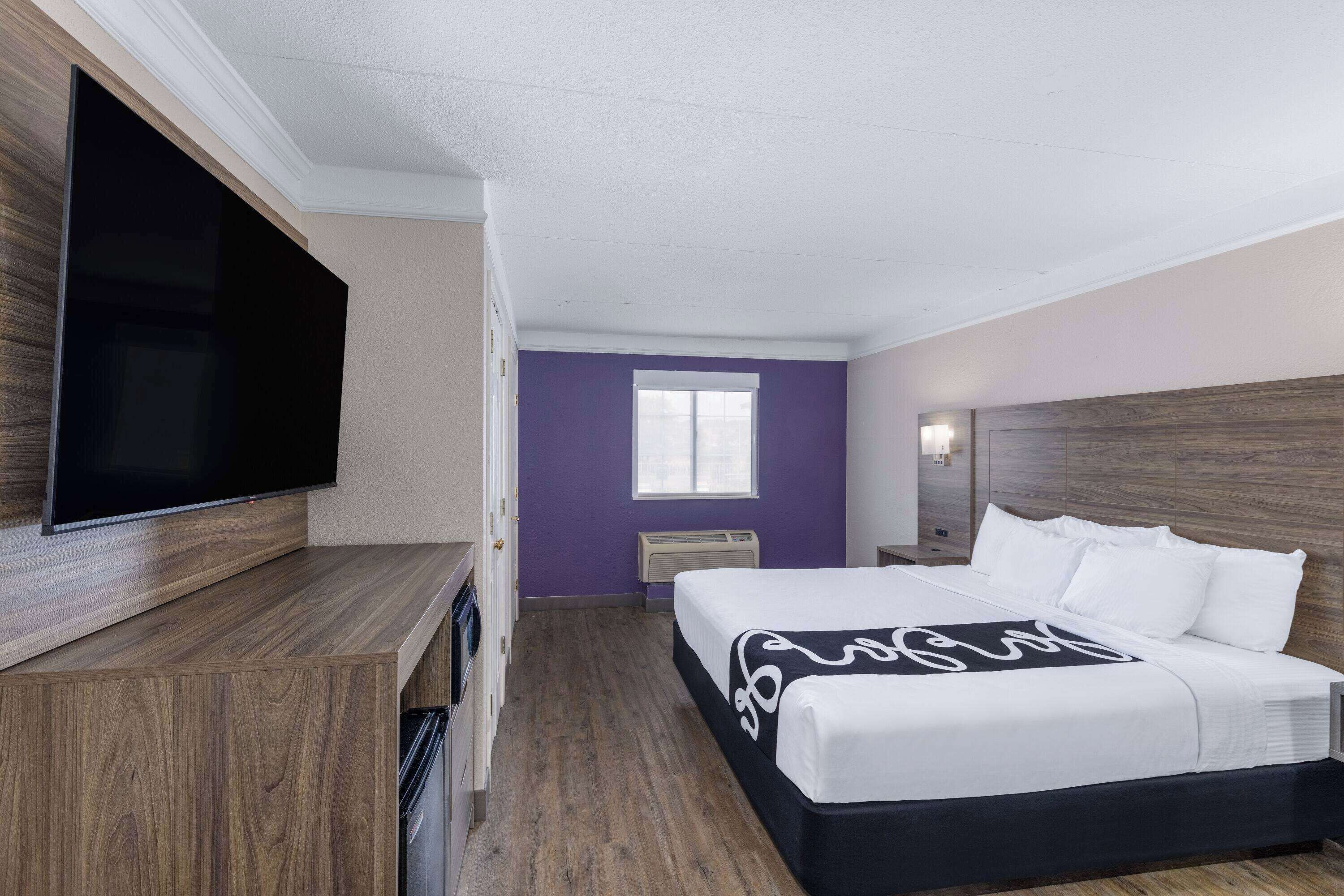 Habitación de hotel con cama, televisión de pantalla plana, ventana y cabecero de madera.