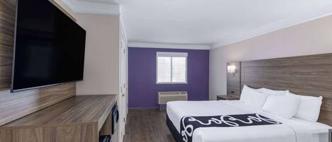 Habitación de hotel con cama, televisión de pantalla plana, ventana y cabecero de madera.
