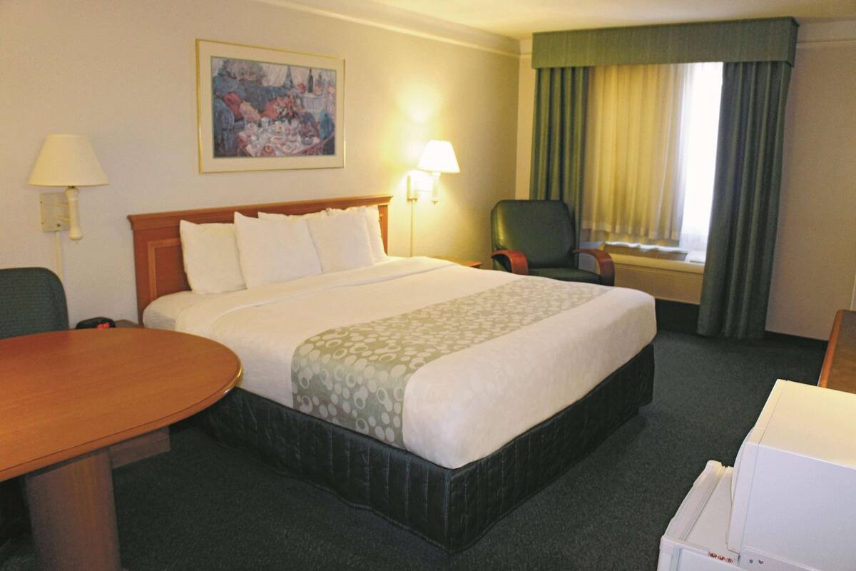 A hotel room with a large bed, a desk, a chair, a lamp, and a painting on the wall.
