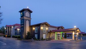 Un hotel con una llamativa torre de reloj, un acceso cubierto y un estacionamiento.