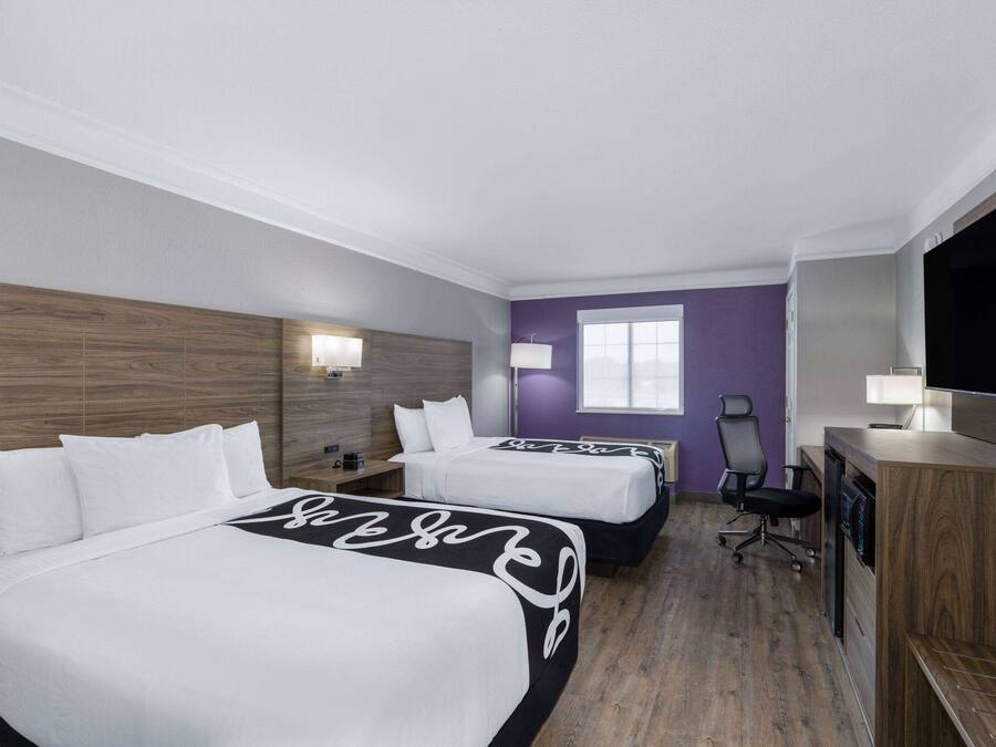 Habitación de hotel con dos camas, un escritorio, una silla, un televisor y una ventana.