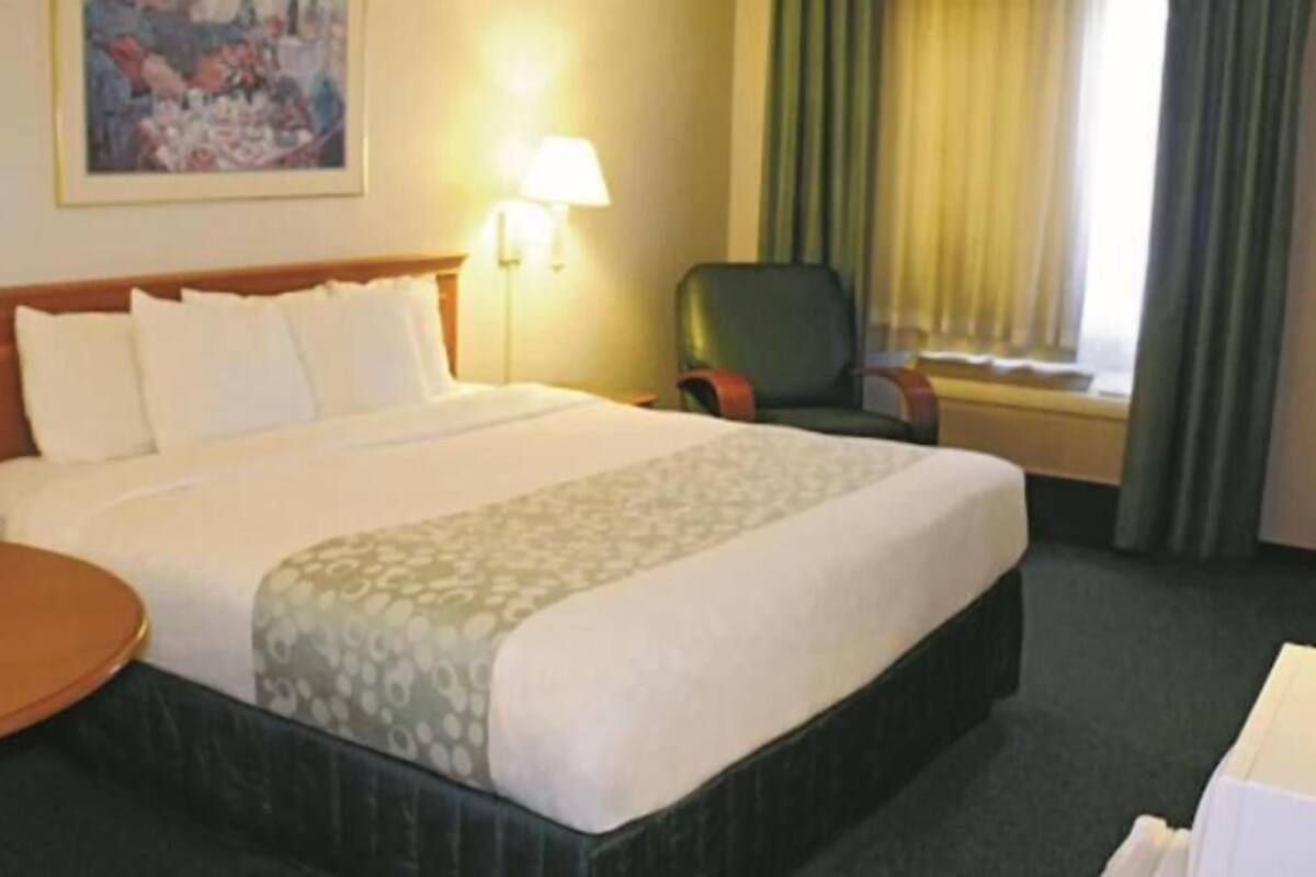 A hotel room with a bed, a desk, a chair, a lamp, and a painting on the wall.