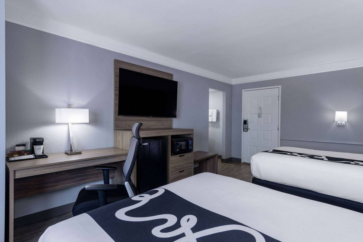 A hotel room with a bed, desk, chair, TV, microwave, and a lamp.