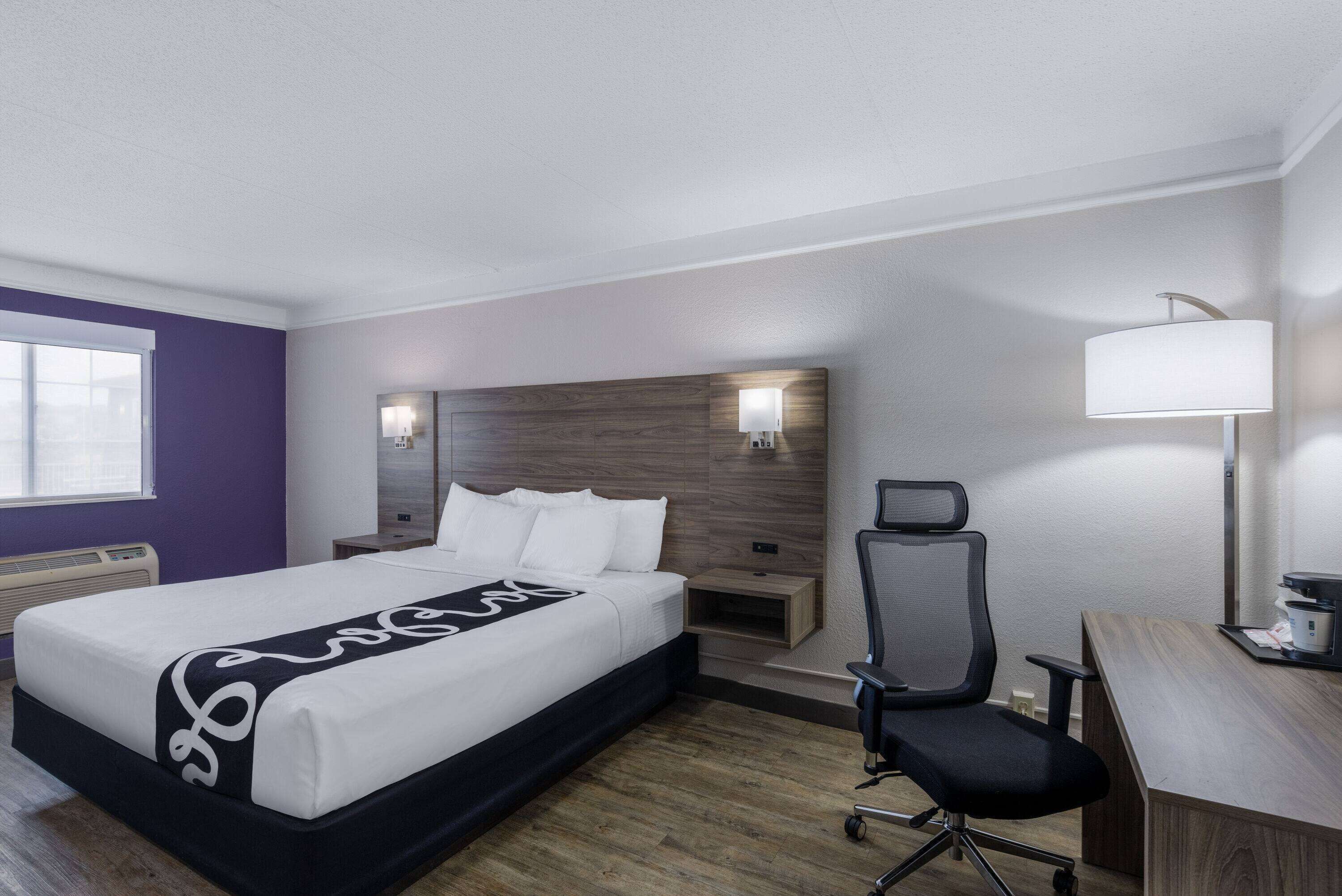 Una habitación de hotel con cama, escritorio, silla, lámpara y mesita de noche.
