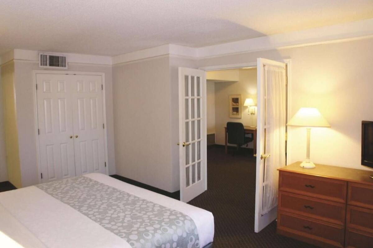 A hotel room with a bed, a desk, a chair, a dresser, and a television.