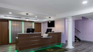 Un mostrador de recepción con detalles de madera, una pared iluminada con luz LED verde y un felpudo con el logotipo de La Quinta.