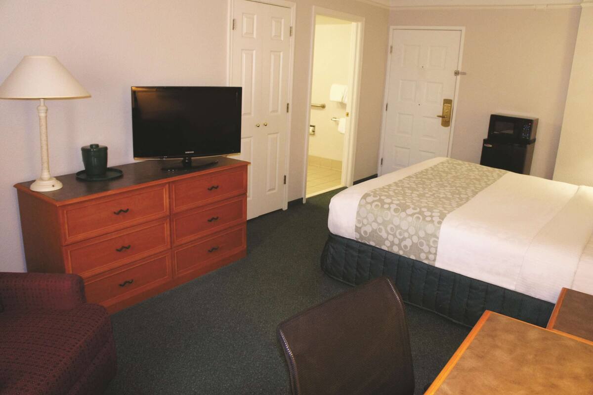 A hotel room with a bed, a television on a wooden dresser, a desk with a chair, and a microwave.