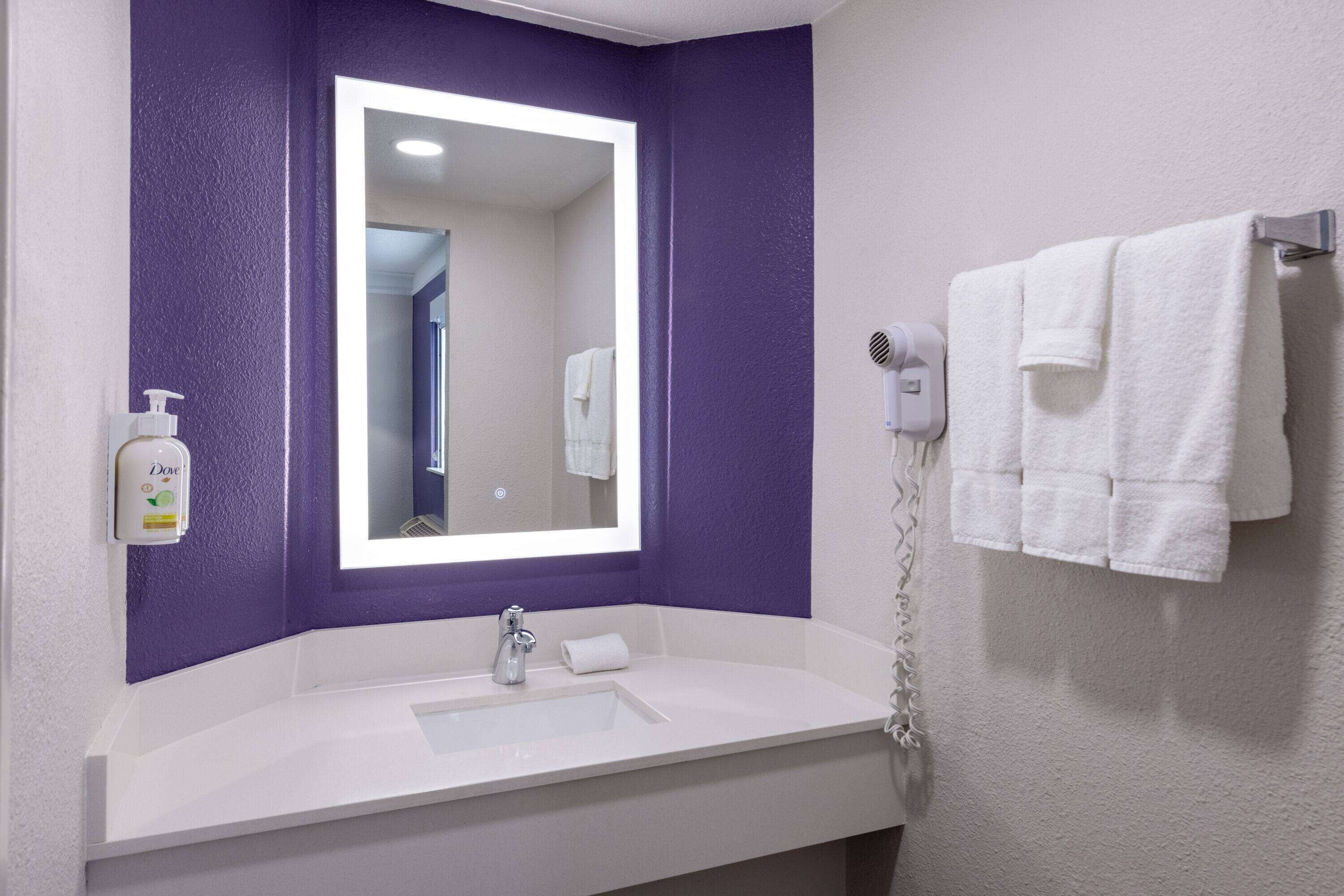 A bathroom with a white sink, purple walls, a mirror, a hairdryer, and a towel rack.