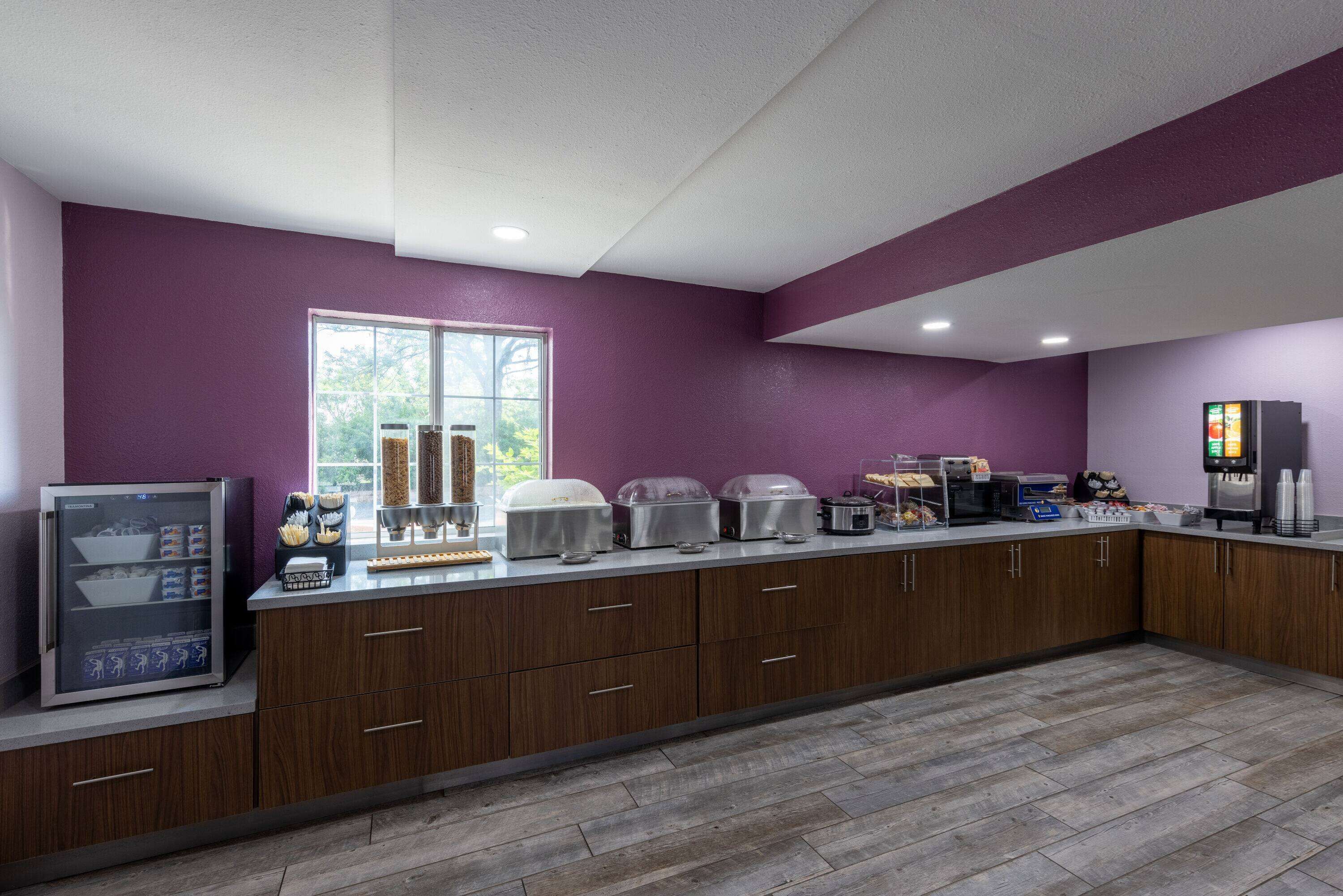 A modern kitchen with purple walls, wooden cabinets, and a large window.