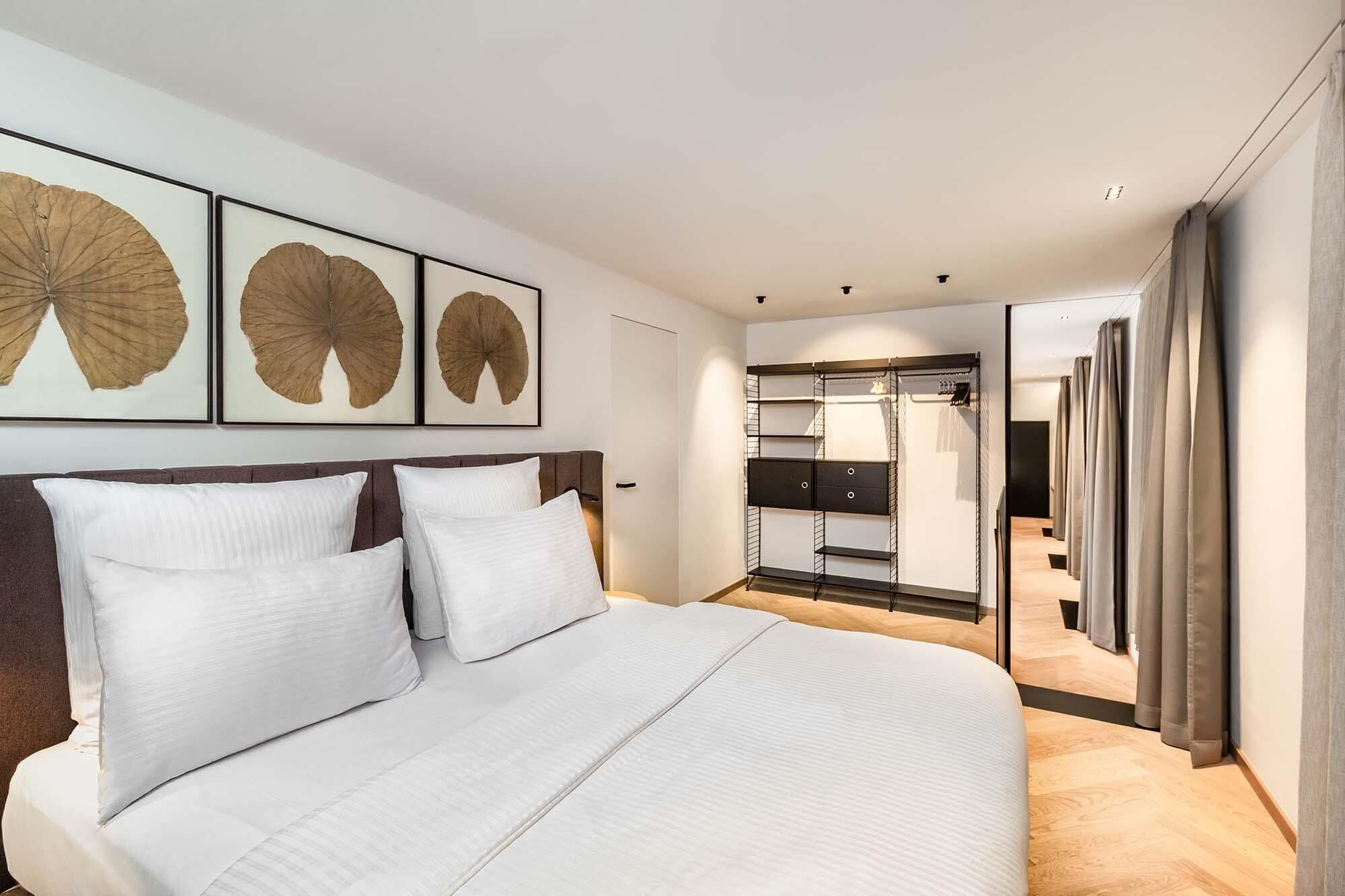 A modern hotel room with a large bed, a walk-in closet, and framed artwork on the wall.