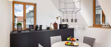 Una cocina moderna con comedor, que cuenta con un amplio ventanal, una lámpara colgante de diseño geométrico y una mesa redonda con sillas.