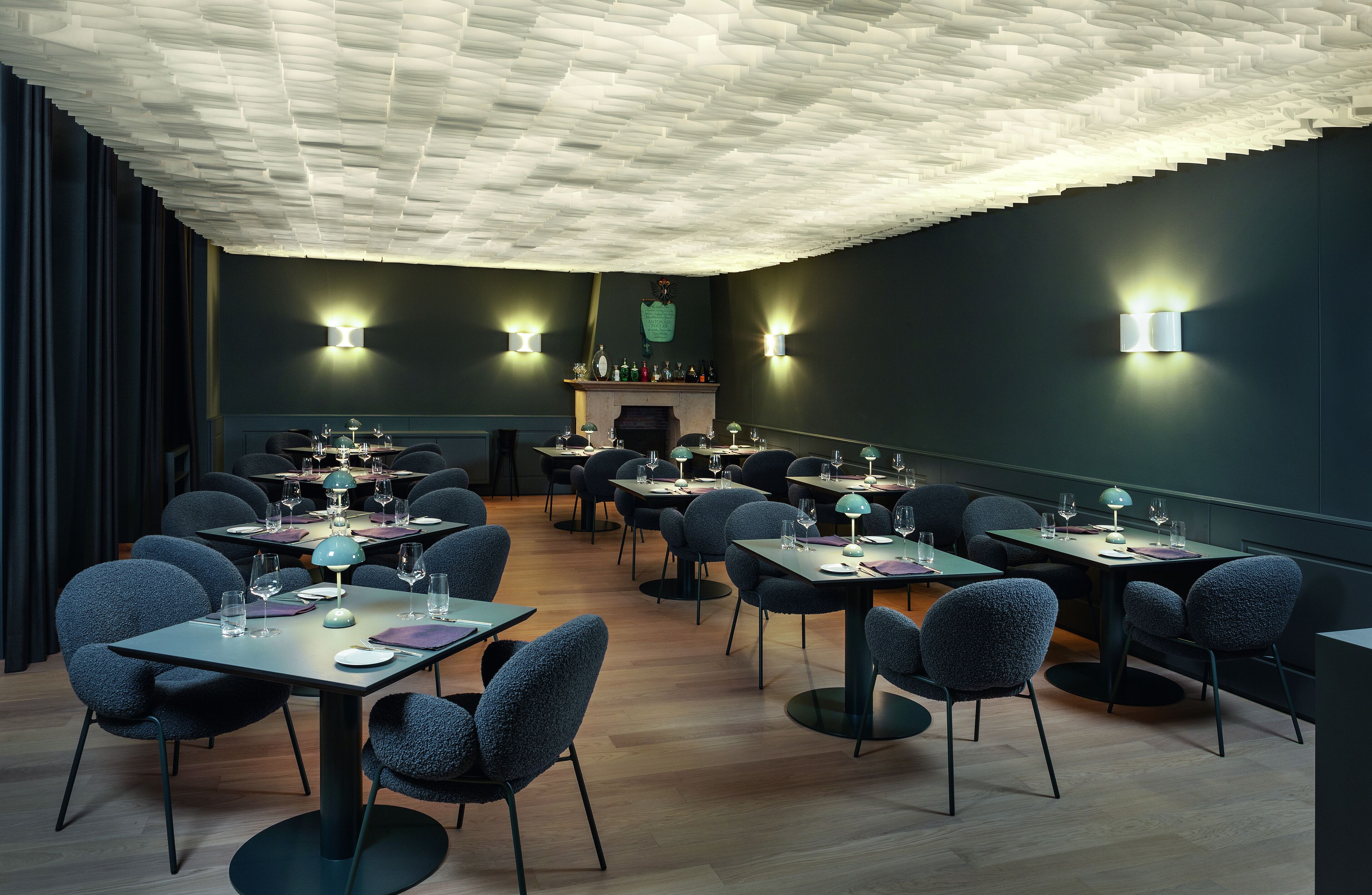 Un comedor moderno con varias mesas y sillas, iluminación ambiental y un diseño de techo único.