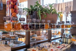 A breakfast buffet with various jams and preserves, including apricots and cherries, and a coffee station.