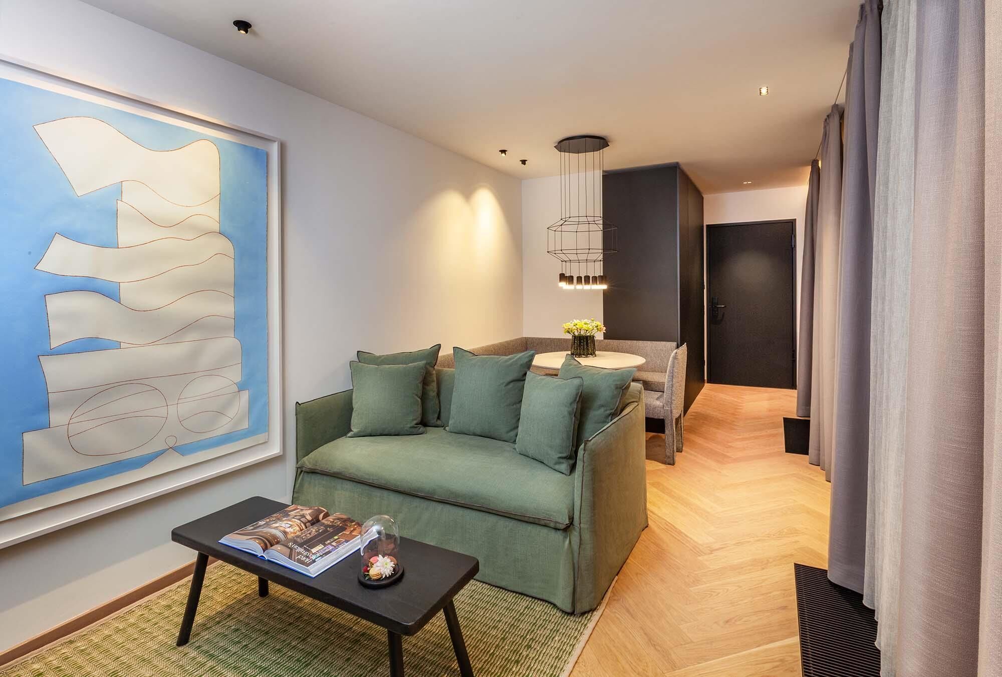 Una sala de estar moderna con un sofá verde, una mesita de centro y un cuadro abstracto grande.