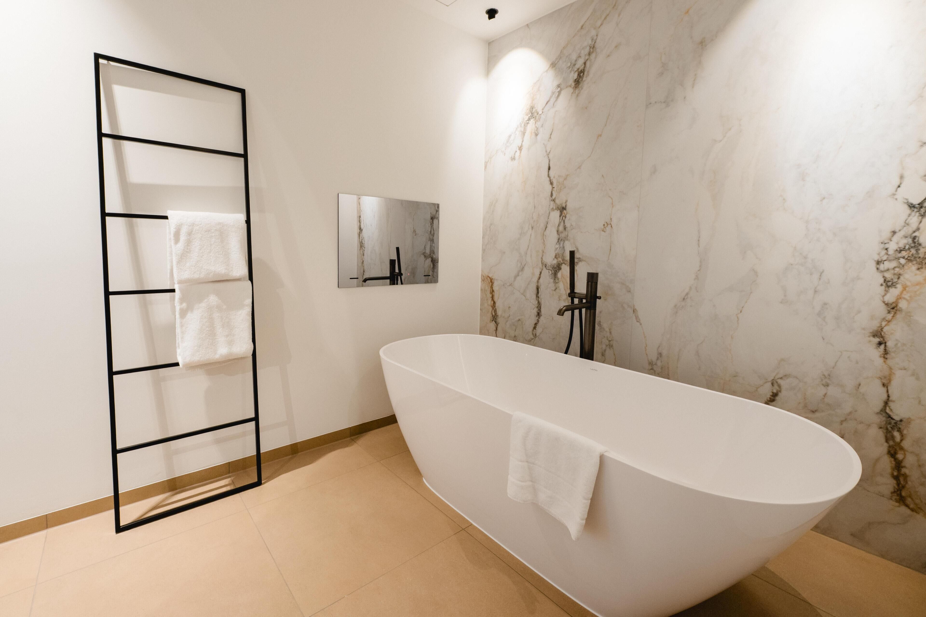 Un baño moderno con una bañera independiente, un perchero, un espejo y una pared de mármol.