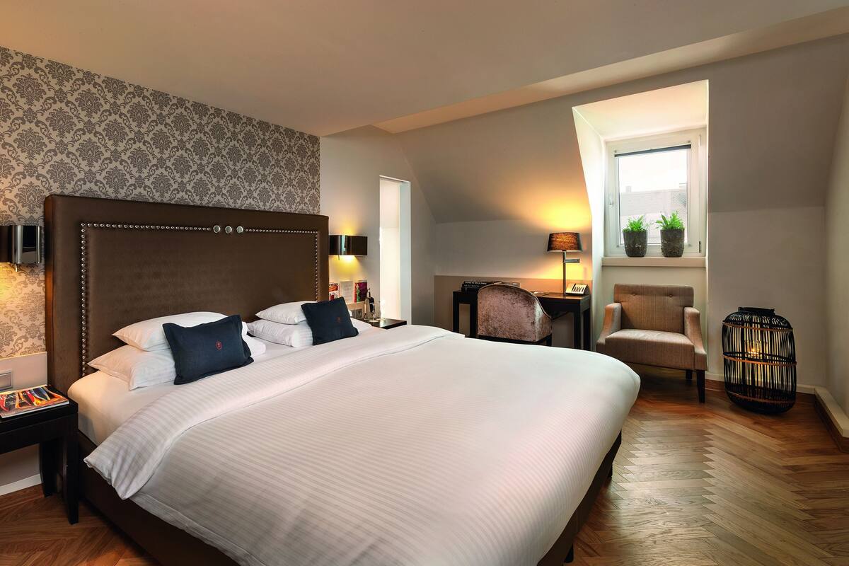 A hotel room with a large bed, bedside tables, a desk, a chair, and a window with a view.