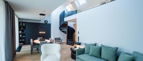 Een modern interieur met een gebogen trap, een groene bank, een witte fauteuil en een eethoek met een ronde tafel.